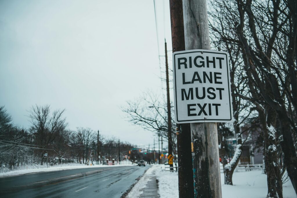 Street sign reading 'Right Lane Must Exit' on snowy urban road in winter.